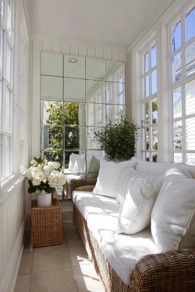Large wall mirror reflecting windows and doubling perceived space in a small sunroom
