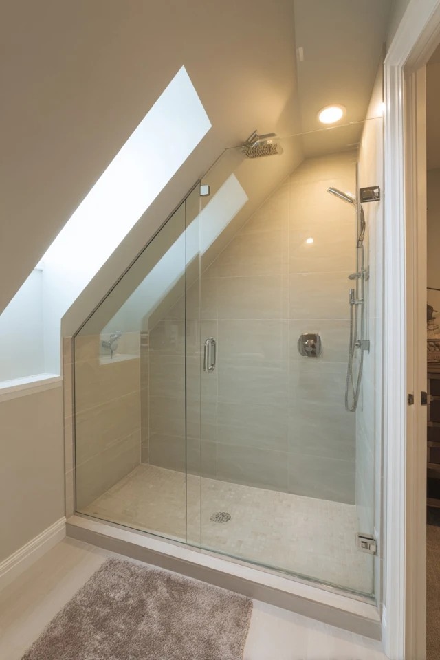Frameless glass shower enclosure fitted beneath the attic slope in a modern functional attic bathroom