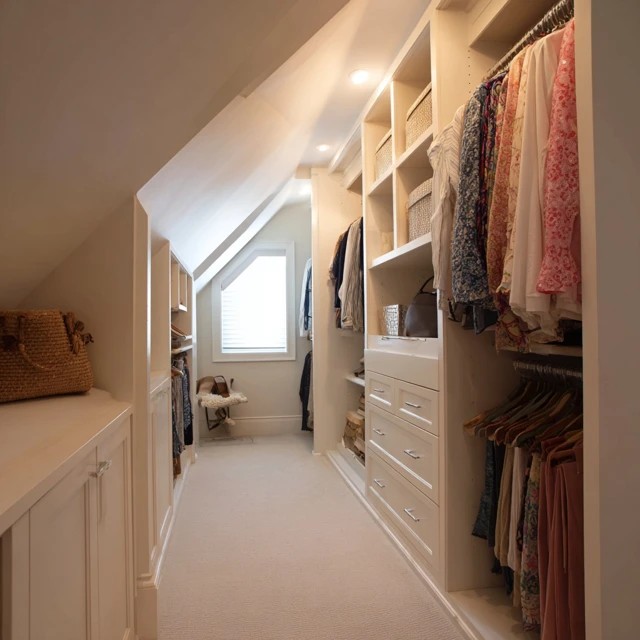 Custom built-in dresser fitted beneath the attic slope providing seamless low-profile storage in the walk-in closet